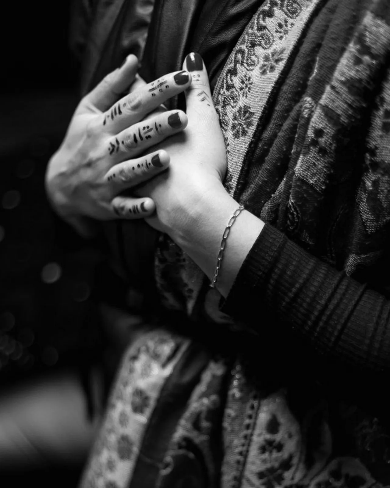 Les mains d’Anissa Lalahoum, tatouées au henné, posées l’une sur l’autre sur un châle brodé.