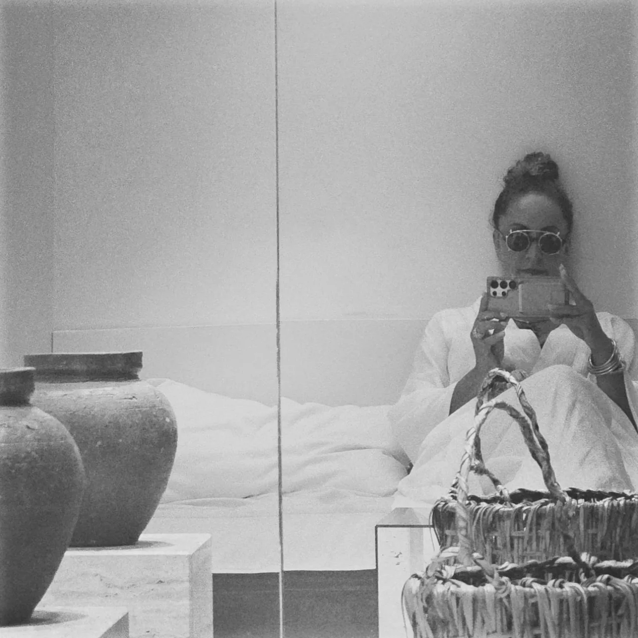 Anissa Lalahoum assise, lunettes de soleil, le téléphone à la main, deux grandes jarres au premier plan.