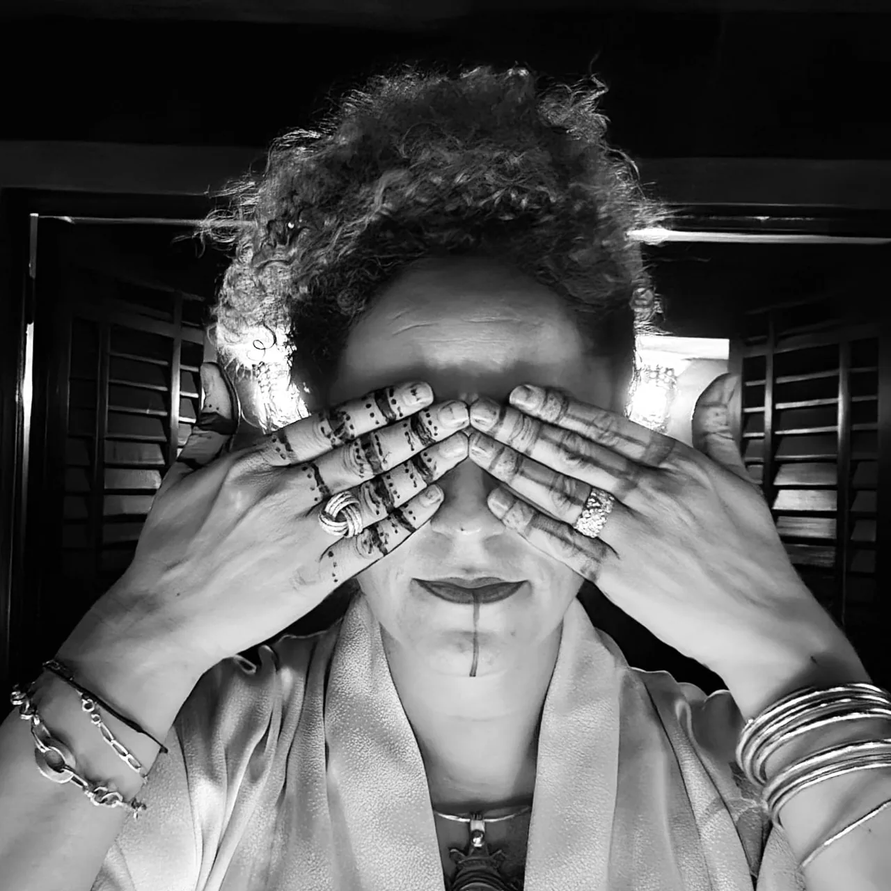 Anissa Lalahoum en noir et blanc, les deux mains tatouées au henné posées sur les yeux.