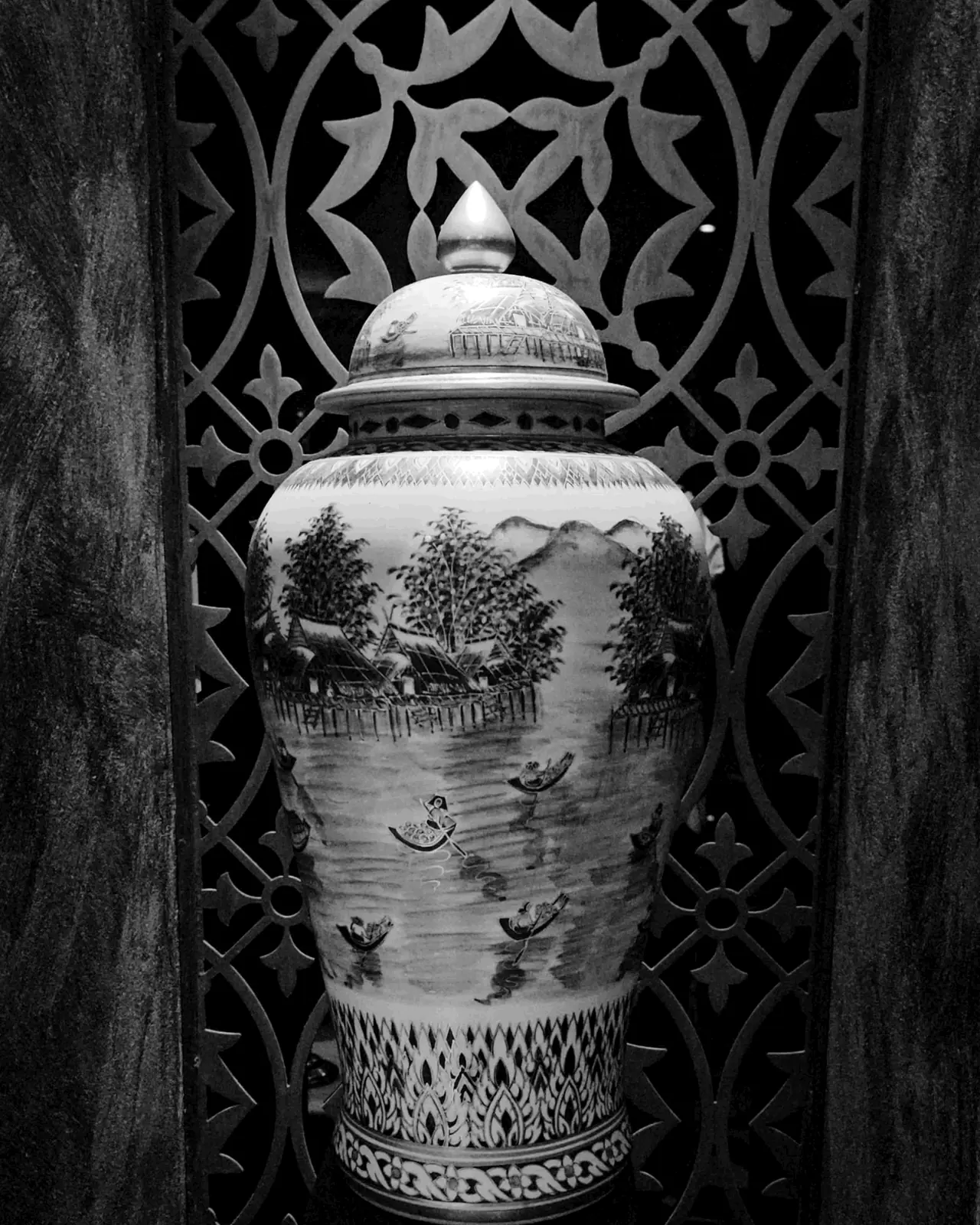 Une jarre de porcelaine peinte, derrière un moucharabieh de bois sculpté, en noir et blanc.